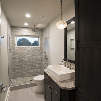 Modern bathroom with a glass-enclosed shower, textured tile wall, single vanity, and a large mirror.