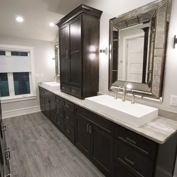 Modern bathroom with double sinks, dark wood cabinets, large mirrors, and gray tile flooring.