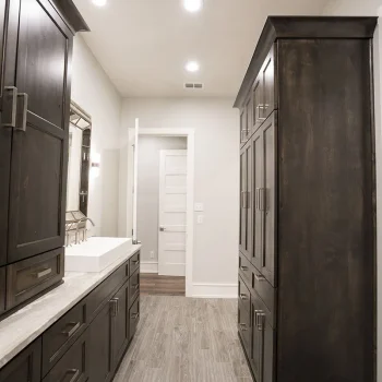 Modern bathroom with dark wood cabinets, double sinks, marble countertop, and light wood-look tile flooring.