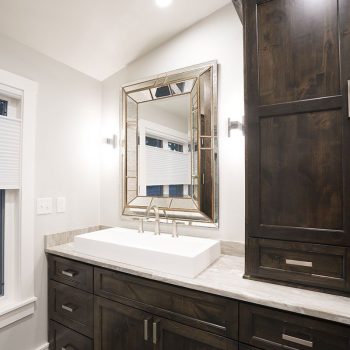 Modern bathroom with dark wood cabinets, a white rectangular sink, large mirror, and overhead lighting.