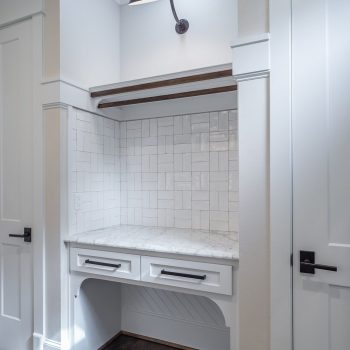 Small built-in desk nook with white tile backsplash, marble countertop, two drawers, and overhead wall sconce lighting.