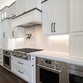 Modern kitchen with white cabinets, stainless steel appliances, gas stove, and marble backsplash.
