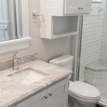 Modern bathroom with a marble countertop, white cabinetry, toilet, and a glass-enclosed shower with subway tile.