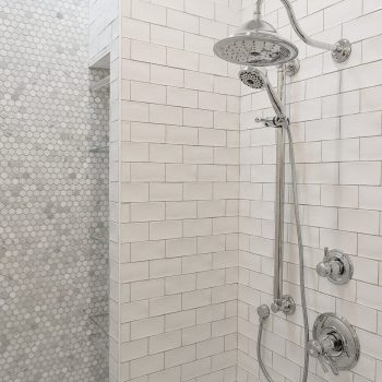 Modern shower with chrome fixtures, handheld showerhead, and white subway tile walls; hexagonal tile accent wall visible.