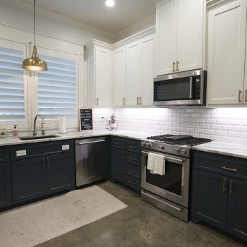 Modern kitchen with dark lower cabinets, white upper cabinets, stainless steel appliances, and subway tile backsplash.