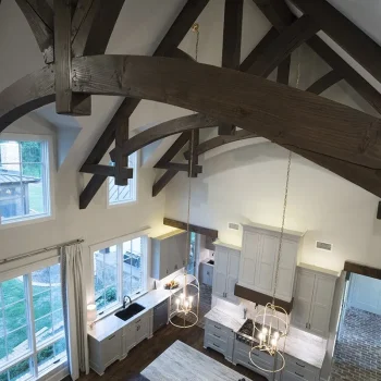 A modern kitchen with vaulted ceilings, exposed wooden beams, white cabinets, and an island with pendant lighting.