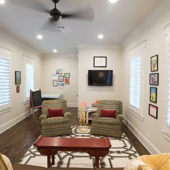 A cozy living room with two armchairs, a TV on the wall, children's toys, and framed artwork decorating the walls.