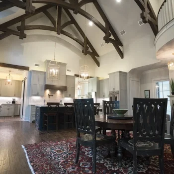 Spacious kitchen and dining area with exposed wood beams, pendant lighting, and a patterned rug on hardwood floors.