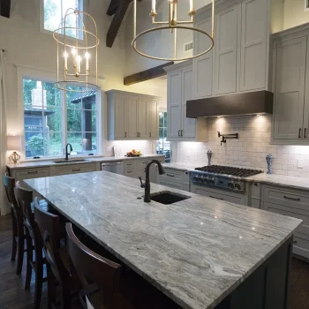 Modern kitchen with marble island, gray cabinets, stainless steel appliances, pendant lights, and large windows.