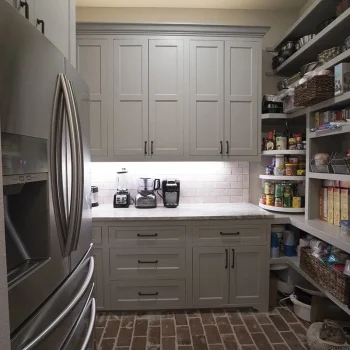 A modern pantry with gray cabinets, countertop appliances, and organized shelves stocked with food and kitchen items.