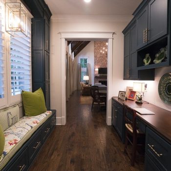 A hallway with a built-in desk, cabinets, bench seating with green pillows, and a view into a living room.