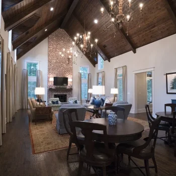Spacious living room with vaulted wooden ceiling, brick fireplace, chandeliers, and seating areas with dark wood furniture.