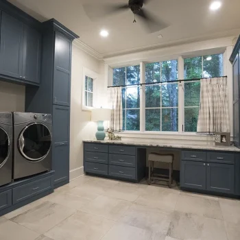 Spacious laundry room with blue cabinets, front-load washer and dryer, large windows, countertops, and a small desk.
