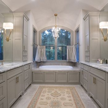 Spacious bathroom with double vanities, marble countertops, a central bathtub, large windows, and elegant light fixtures.