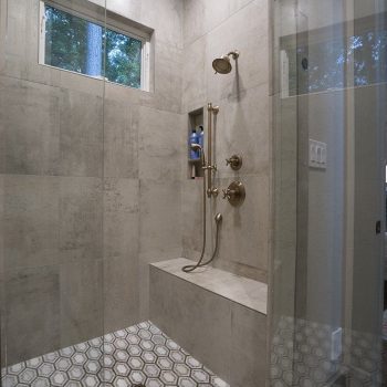 Modern walk-in shower with gray tile walls, built-in bench, hexagonal tile floor, and a window above.