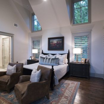 A bedroom with a large bed, two armchairs, bedside tables with lamps, and windows above the bed.