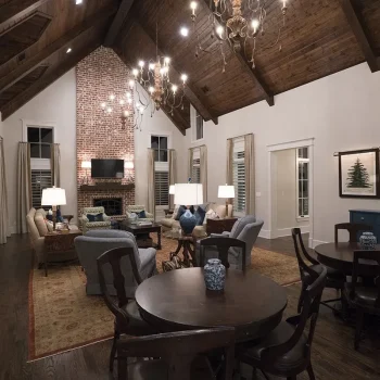Spacious living room with vaulted wood ceiling, brick fireplace, sofas, round tables, and wall art.