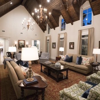 Spacious living room with vaulted wooden ceiling, sofas, armchairs, lamps, and large windows with drapes.