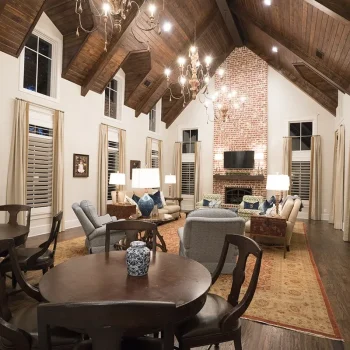 Spacious living room with vaulted wood ceiling, brick fireplace, large windows, and mixed seating arrangements.