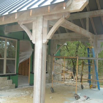 Partially constructed house with exposed wooden beams, scaffolding, and a window; construction materials are visible.