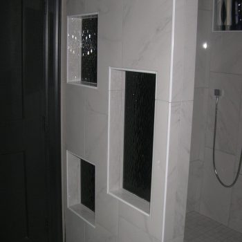 Modern shower area with a tiled wall, three glass block windows, and a handheld showerhead.