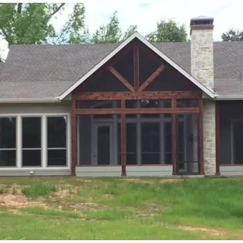 Single-story house with large windows, a stone chimney, and a screened-in porch, set on a grassy lawn with trees behind.