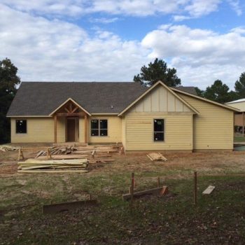 A single-story house under construction with unfinished yard and building materials in front.