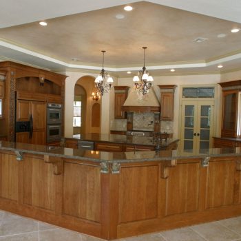 Spacious kitchen with wood cabinetry, granite countertops, built-in appliances, and tile flooring under recessed lighting.