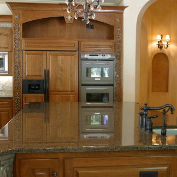Modern kitchen with wooden cabinets, granite countertops, built-in appliances, and a small sink on the island.