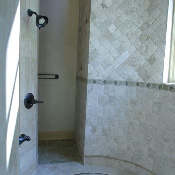 Curved walk-in shower with beige tile walls and floor, black fixtures, and natural light from a window.