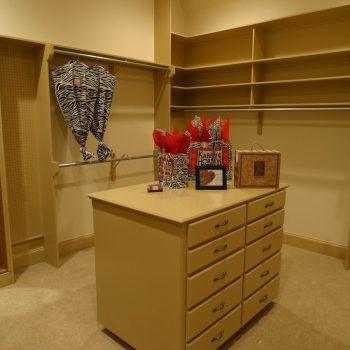 Spacious walk-in closet with an island dresser, wall mirror, shelving, and zebra-print garment bags.