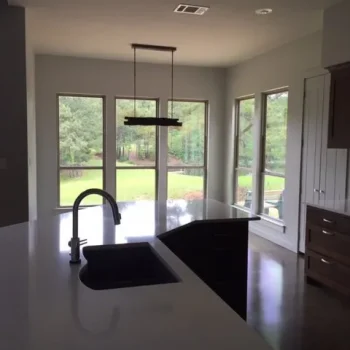 Modern kitchen with dark cabinets, white countertops, and large windows overlooking a green backyard.