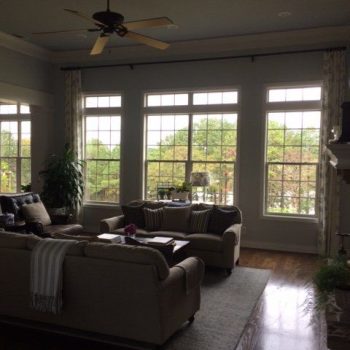 Living room with two sofas, a coffee table, large windows, and hardwood floors, overlooking trees outside.