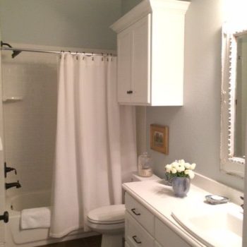 Bathroom with white cabinets, a shower with a white curtain, a toilet, and a sink with a vase of flowers.