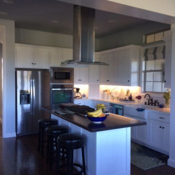 Modern kitchen with white cabinets, stainless steel appliances, a large island with stools, and a bowl of bananas on the counter.