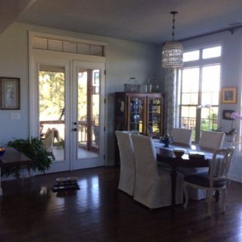Dining room with a wooden table, six chairs, glass cabinet, and large windows letting in natural light.