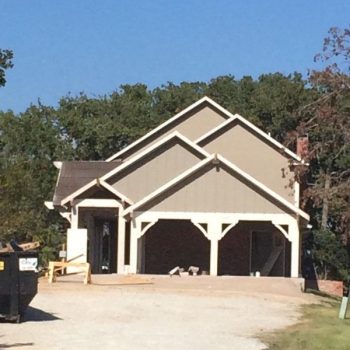 Single-family house with overlapping gabled roofs, open garage, and construction materials in the driveway.