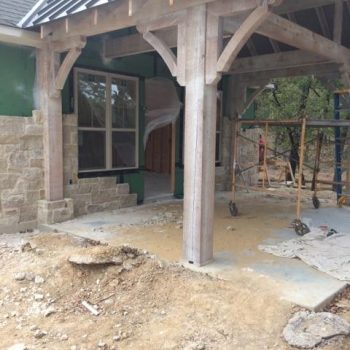 Wood and stone house under construction with scaffolding and unfinished ground in front of a covered entryway.
