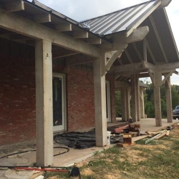 A brick house with a metal roof and exposed wooden beams is under construction with tools and materials scattered outside.