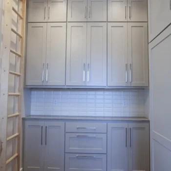A kitchen with light gray cabinets, a tile backsplash, and a wooden ladder mounted on the left wall.