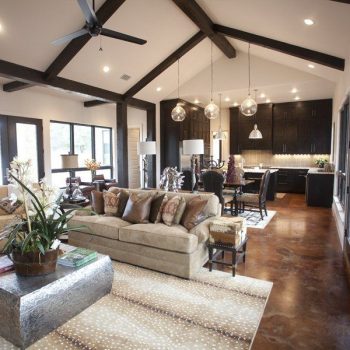 Spacious open-plan living room and kitchen with large windows, exposed beams, modern furniture, and pendant lights.