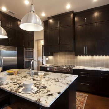 Modern kitchen with dark wood cabinets, stainless steel appliances, marble island, and pendant lights.