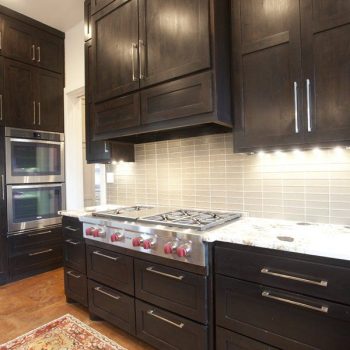 Modern kitchen with dark wood cabinets, stainless steel stove and oven, under-cabinet lighting, and a patterned rug.