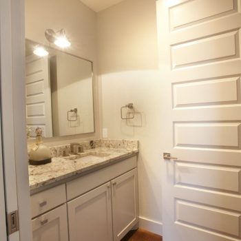 Small bathroom with white cabinets, granite countertop, wall mirror, and open paneled door under ceiling light.