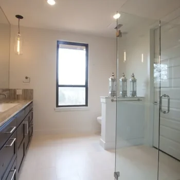 Modern bathroom with glass shower, double sink vanity, large window, and decorative jars on a shelf near the toilet.