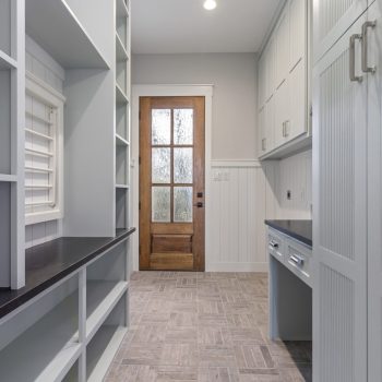 A laundry room with built-in cabinets, a countertop, herringbone tile floor, and a wooden door with glass panels.