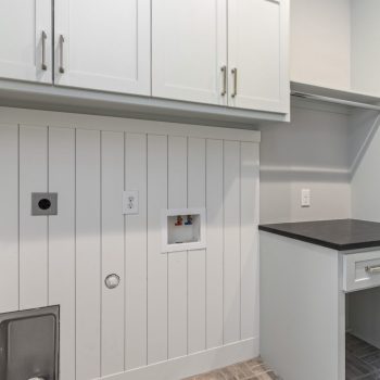 Laundry room with white cabinets, utility hookups, black countertop, drawers, and a small pet door on a paneled wall.