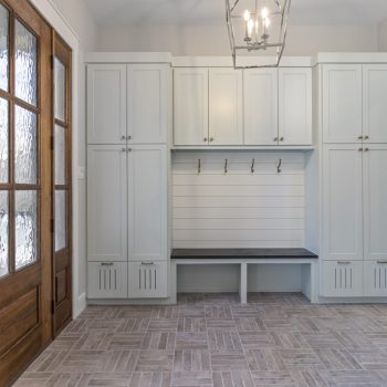 Mudroom with built-in cabinets, coat hooks, bench seating, wood door, and tiled floor.
