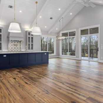 Spacious modern kitchen with large windows, wood floors, navy island, white cabinets, and pendant lights.