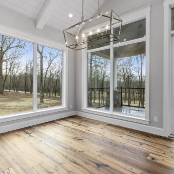 Empty room with large windows, wood floors, modern light fixture, and view of trees and a balcony outside.